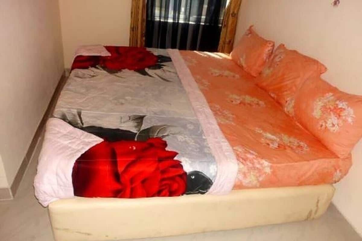 A bed with a floral bedspread, a red blanket, and a white pillow.