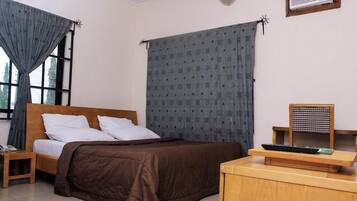 Un dormitorio con cama, mesita de noche, escritorio con silla, ventana con cortinas y aire acondicionado instalado en la pared.