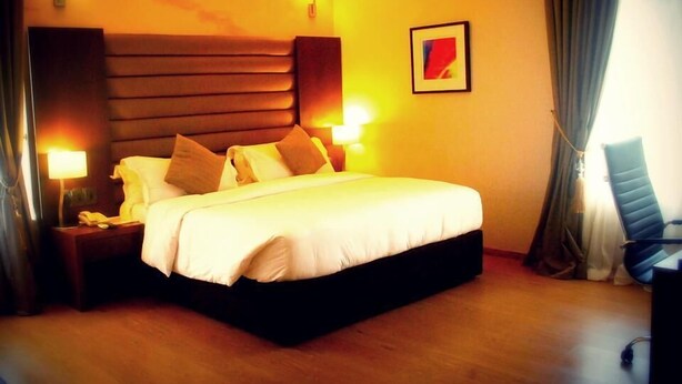 A hotel room with a large bed, bedside lamps, a chair, and a framed picture on the wall. - Sweet Dreams Hotel (Calabar)