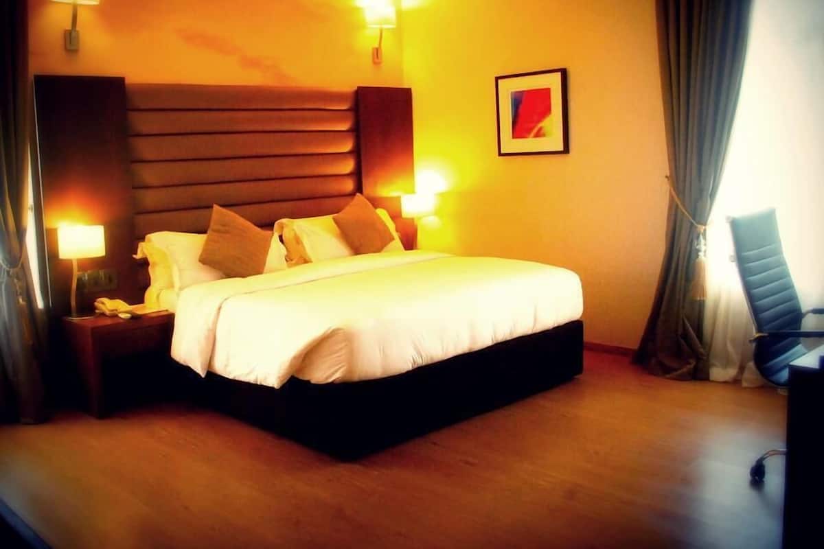 A hotel room with a large bed, bedside lamps, a chair, and a framed picture on the wall.