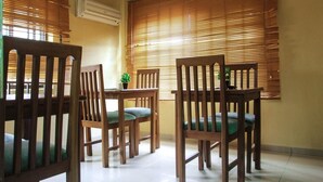 A dining area with wooden chairs and a table, large windows with blinds, and a small potted plant on the table. - Sweet Dreams Hotel (Calabar)