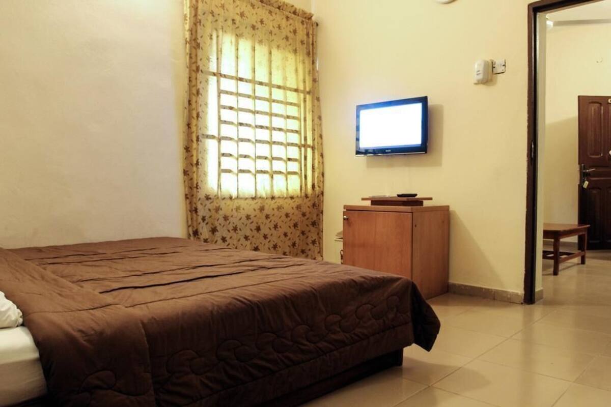 A bedroom with a bed, a television, a wooden cabinet, and a window with curtains.