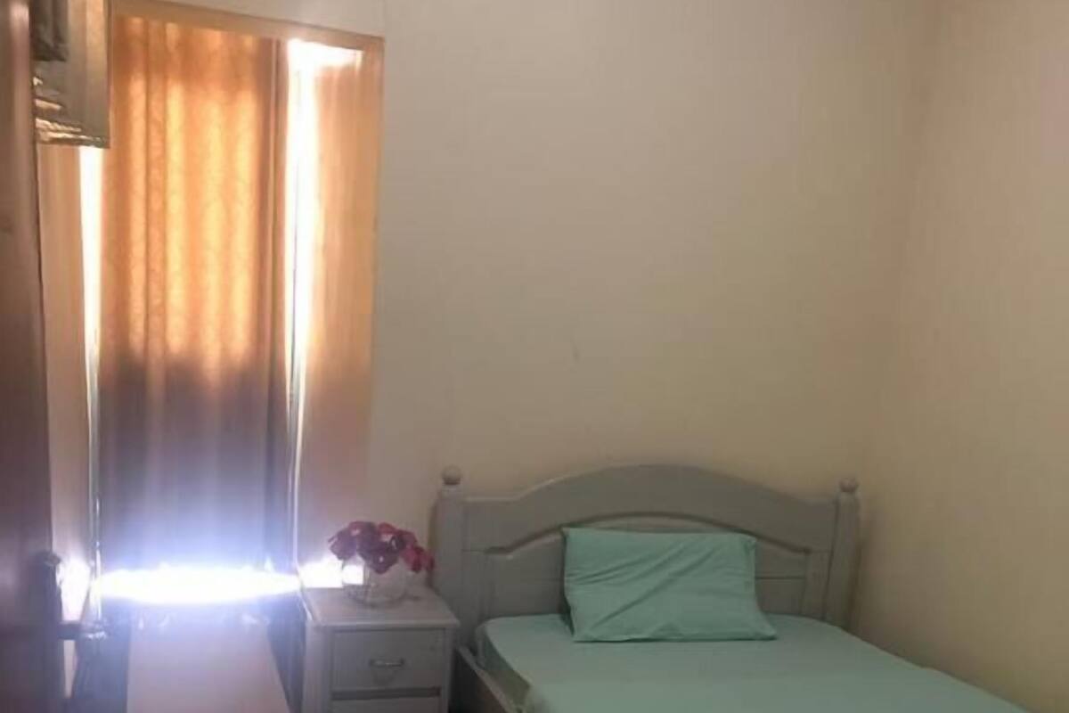 A bedroom with a bed, a nightstand, a dresser, and a window with curtains.