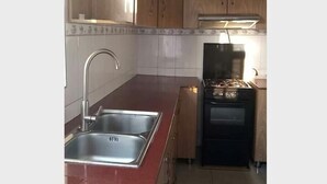 A kitchen with wooden cabinets, a stainless steel sink, a gas stove, and a tiled backsplash. - Nova Apartment (Kigali)