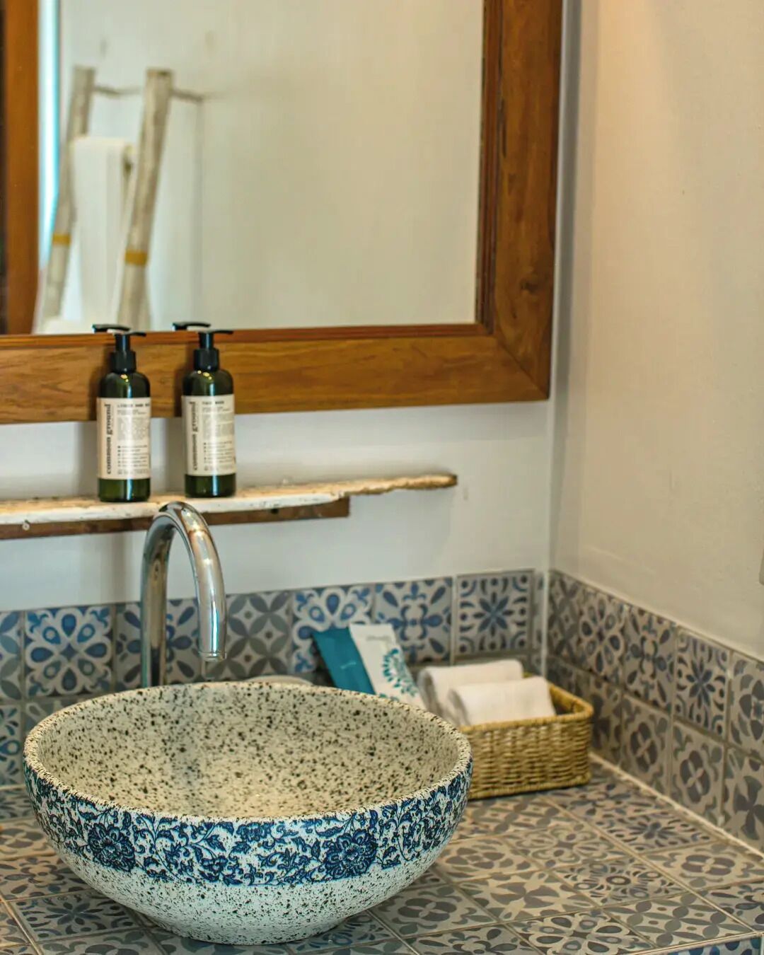 A bathroom with a speckled bowl sink, a mirror, and a shelf with toiletries.