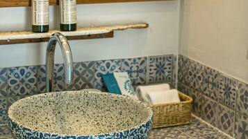 A bathroom with a speckled bowl sink, a mirror, and a shelf with toiletries.