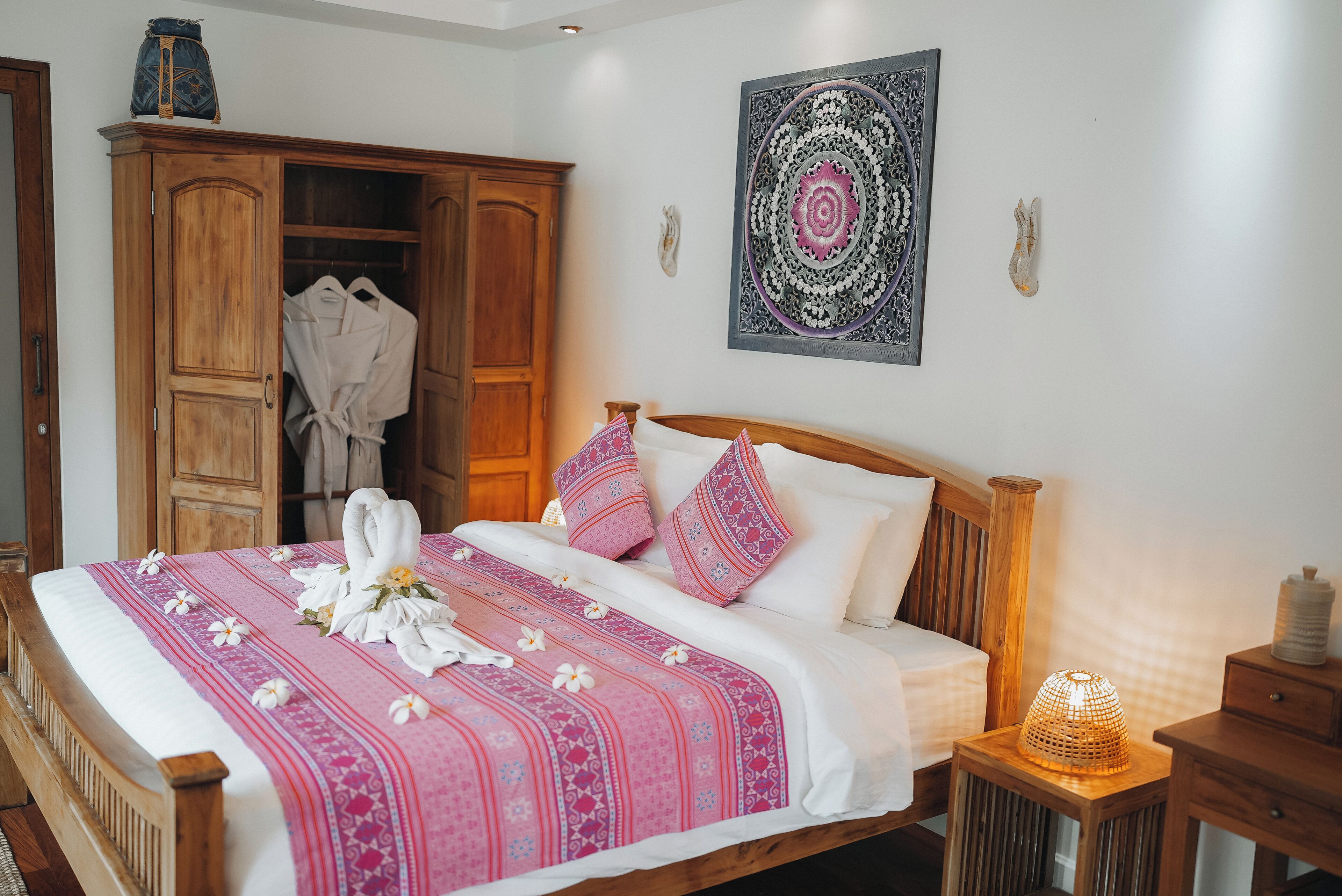 Una cama bien hecha con una colcha estampada en rosa y blanco, un cabecero de madera y una lámpara de noche.