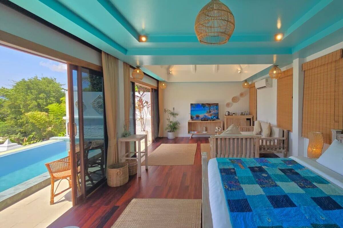 A bedroom with a large bed, a TV, a desk, and a view of a pool.