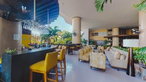 Un espacio lounge moderno con barra, sillas amarillas, sofás y vistas a plantas tropicales.
