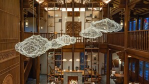 Un hall d’entrée spacieux avec de hauts plafonds, des poutres en bois et des luminaires suspendus.