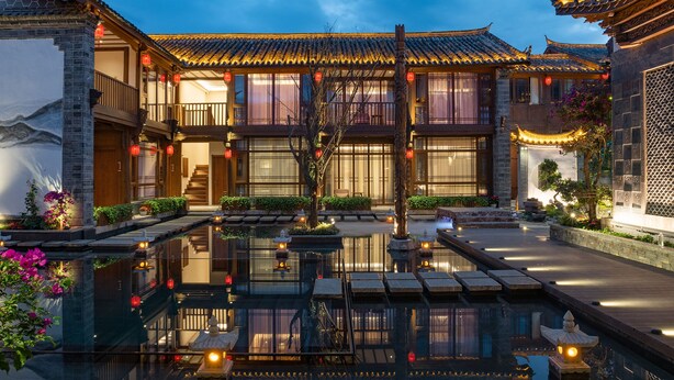 Une cour traditionnelle chinoise agrémentée d’un bassin d’eau décoratif, de bâtiments en bois et de lanternes rouges.