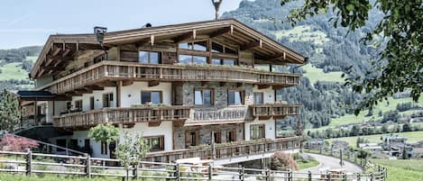 Ein mehrstöckiges Gebäude mit Balkonen, einem Turm und Blick auf eine gebirgige Landschaft.