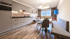A modern kitchen with built-in appliances, a dining area with a table and chairs, a bench, and a TV mounted on the wall. - Secluded Farmhouse in Tyrol near Ski Area (Schwendau)