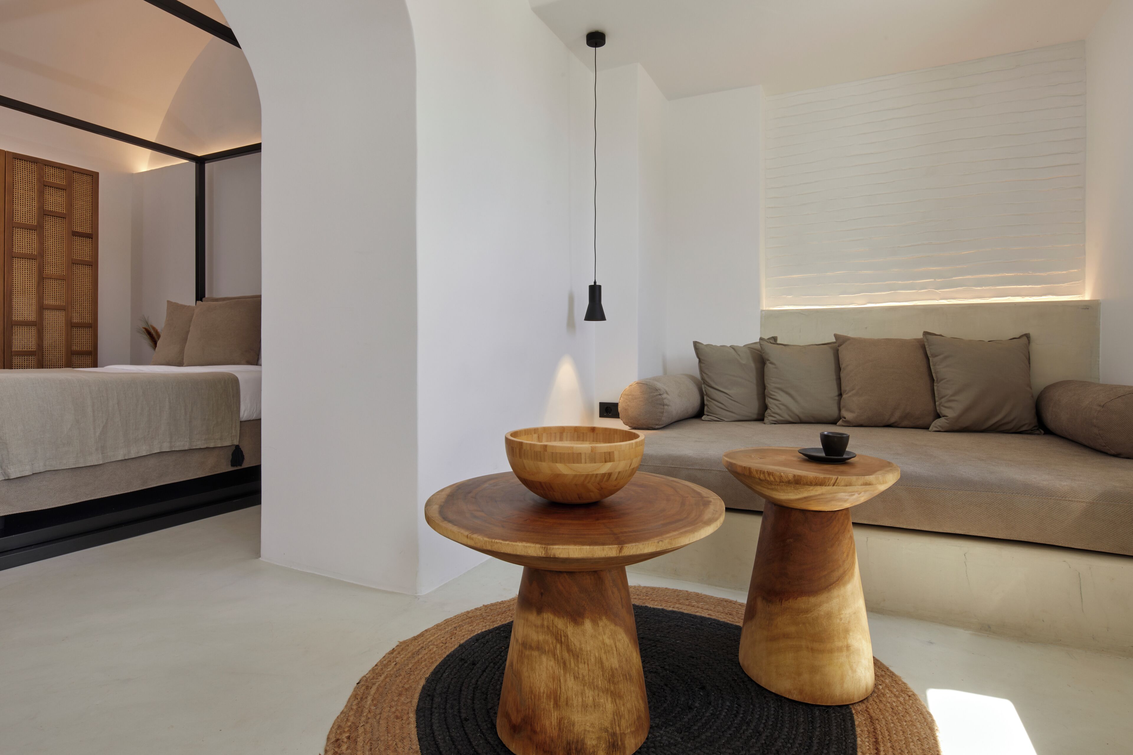 A modern bedroom with a bed, a wooden side table, a round wooden table, and a sofa with cushions.