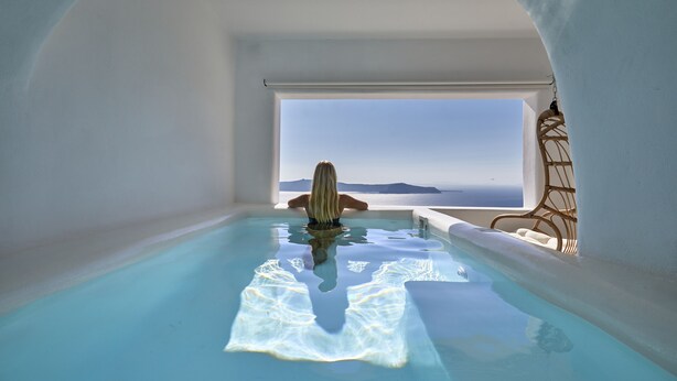 A person in a clear pool with a view of the sea. - You And Me Suites (Santorini)