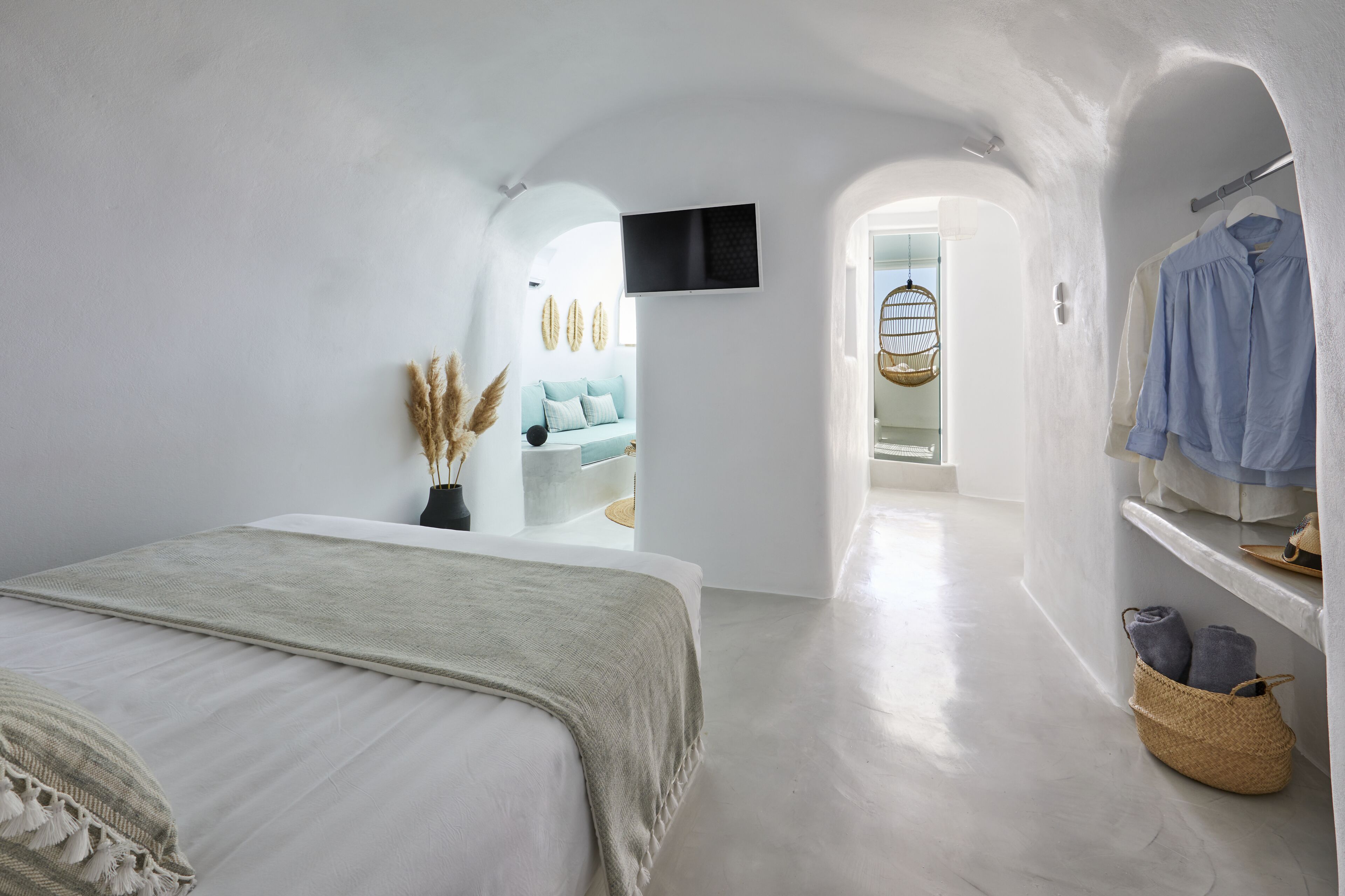 A minimalist bedroom with a bed, a TV mounted on the wall, and a walk-in closet with hanging clothes.