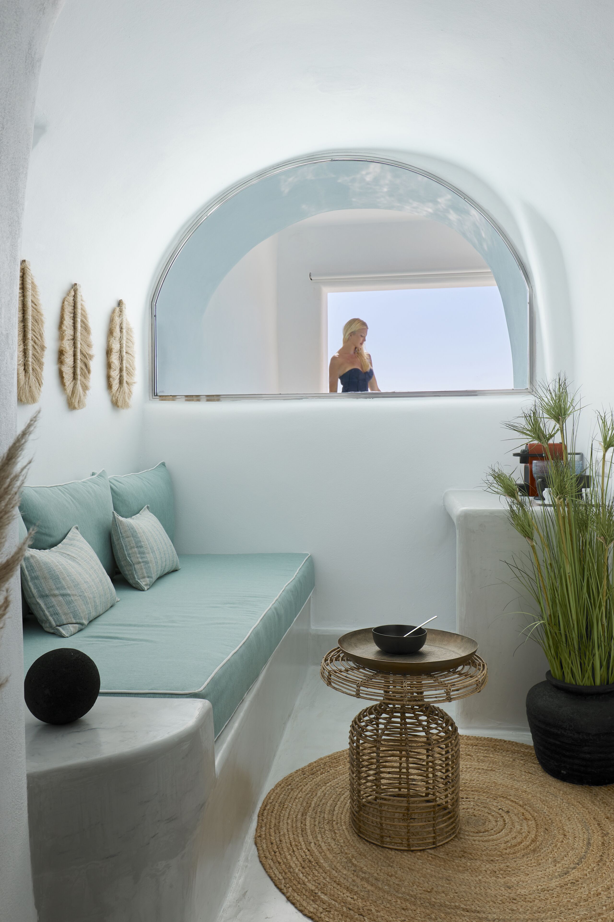 A cozy room with a light blue sofa, a round woven table, and a large mirror above a window.