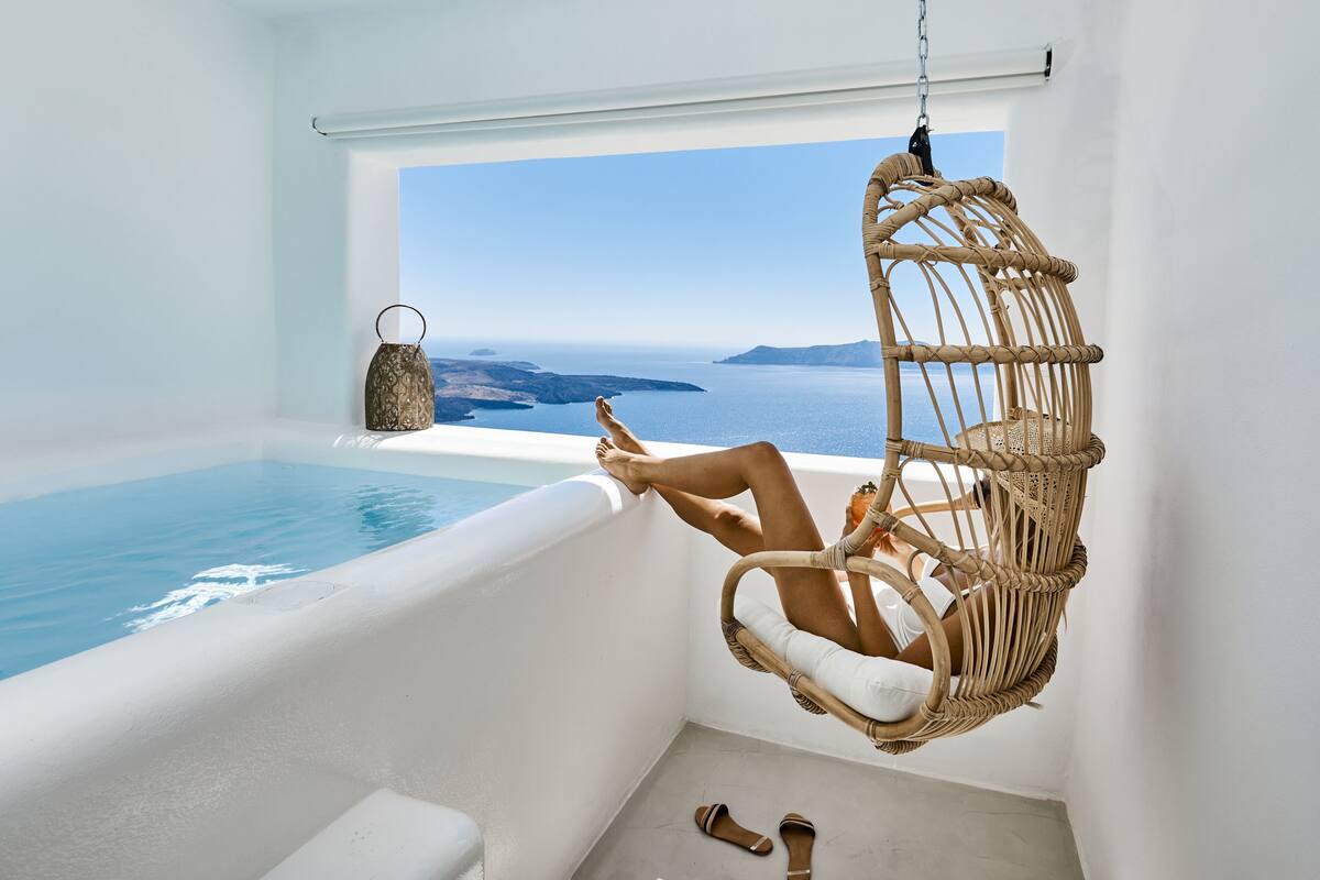 A room with a view of the sea, a hanging chair, a small table, and a bottle.