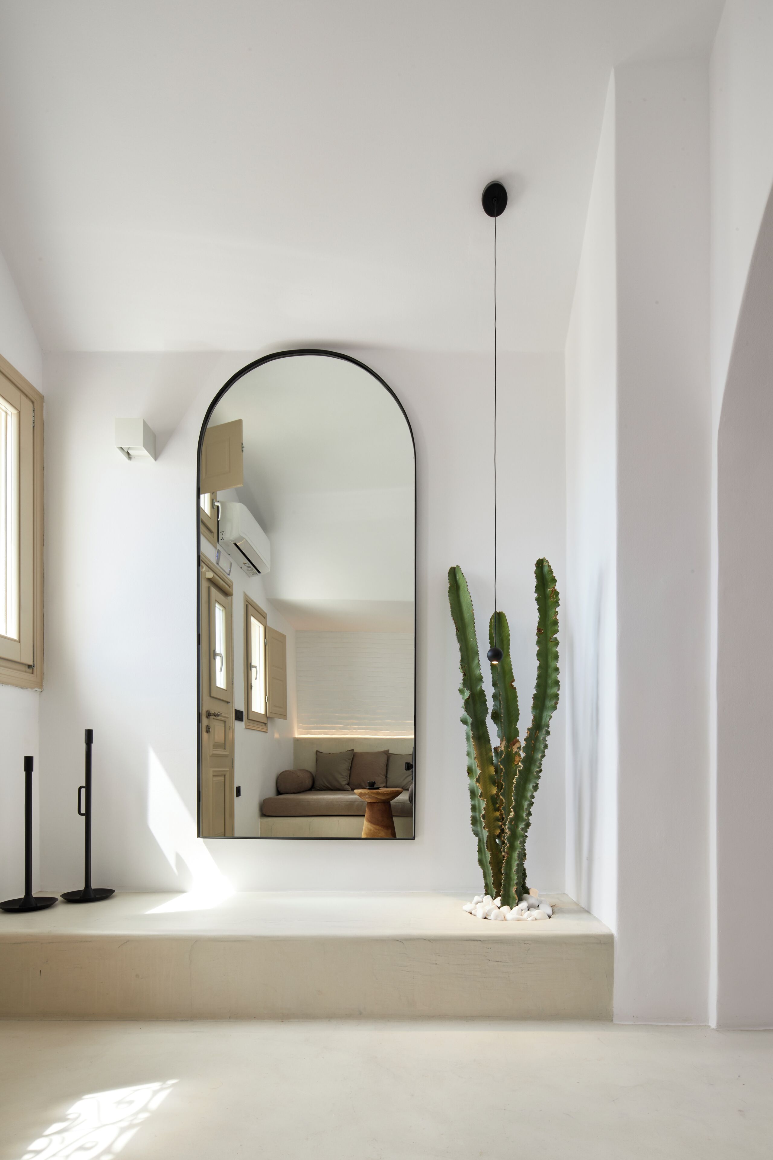 A minimalist room with a large mirror, a cactus, and a small table.