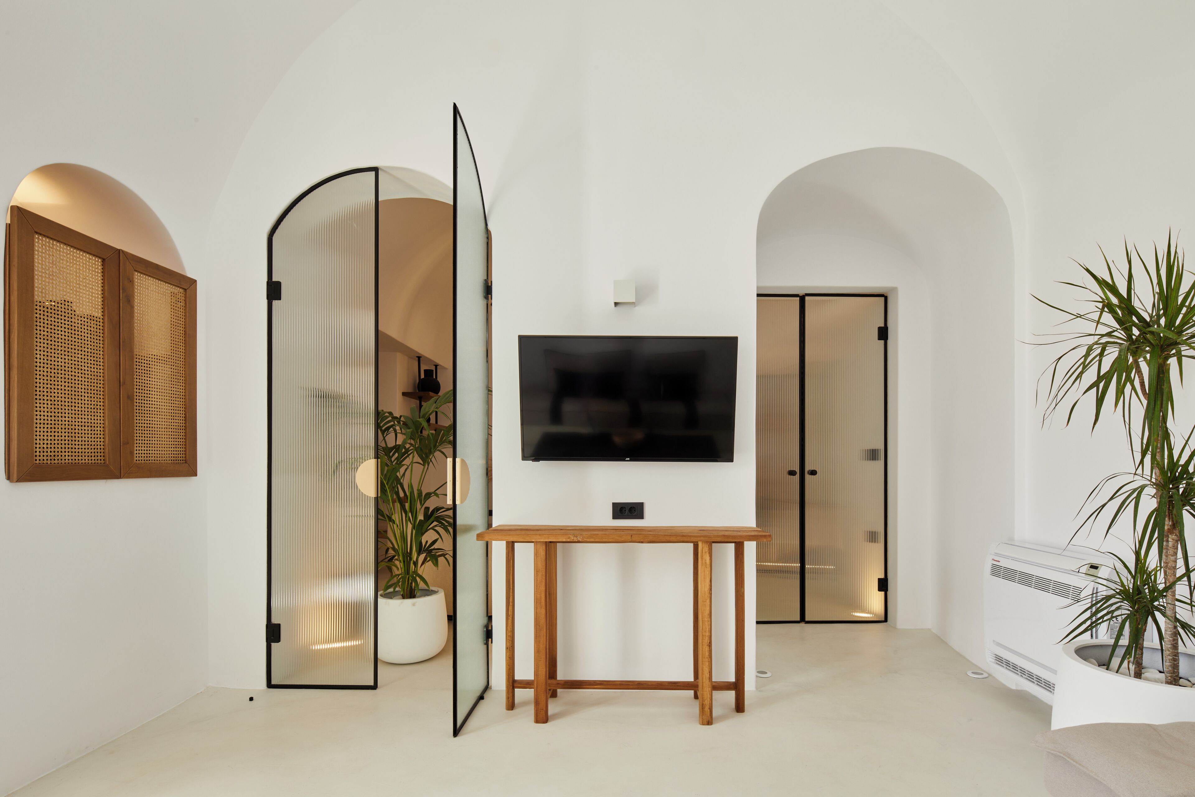 A modern living room with a flat-screen TV, a wooden table, and a potted plant.