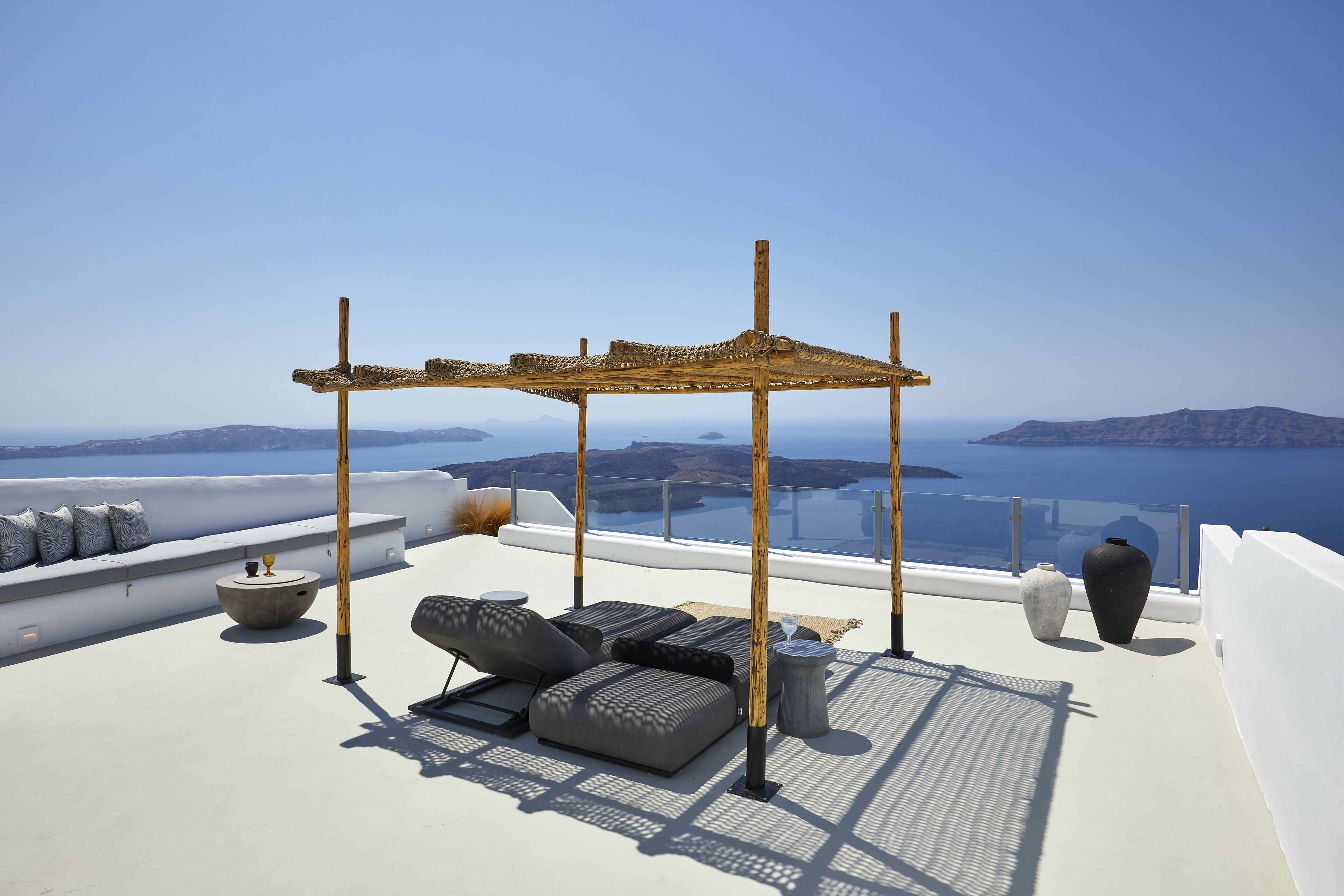 A rooftop terrace with a pergola, lounge chairs, a round table, and two vases.