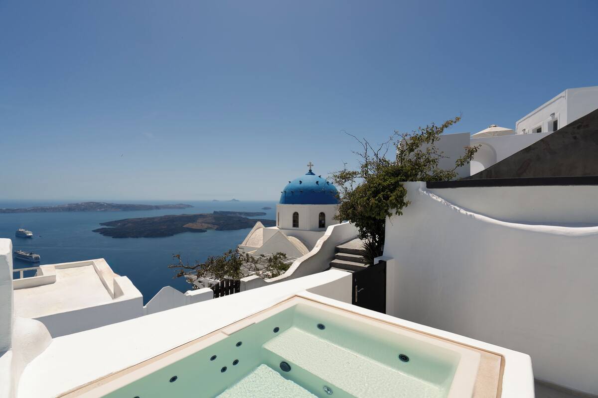 A rooftop pool with a view of the sea and a blue-domed building in the background.