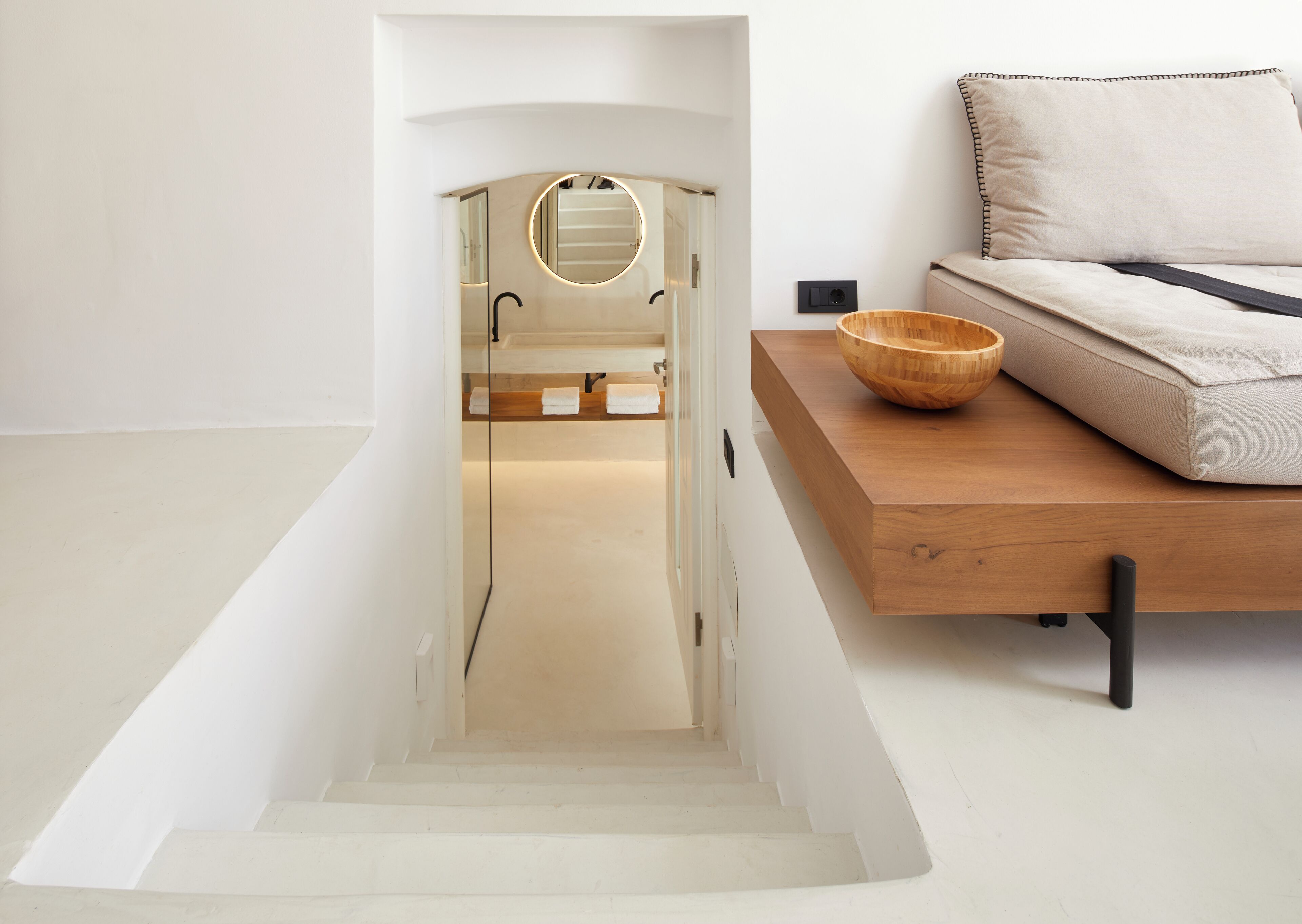 Un intérieur moderne avec un escalier menant à une salle de bain, une table d’appoint en bois sur laquelle se trouve un bol, et un canapé agrémenté d’un coussin.