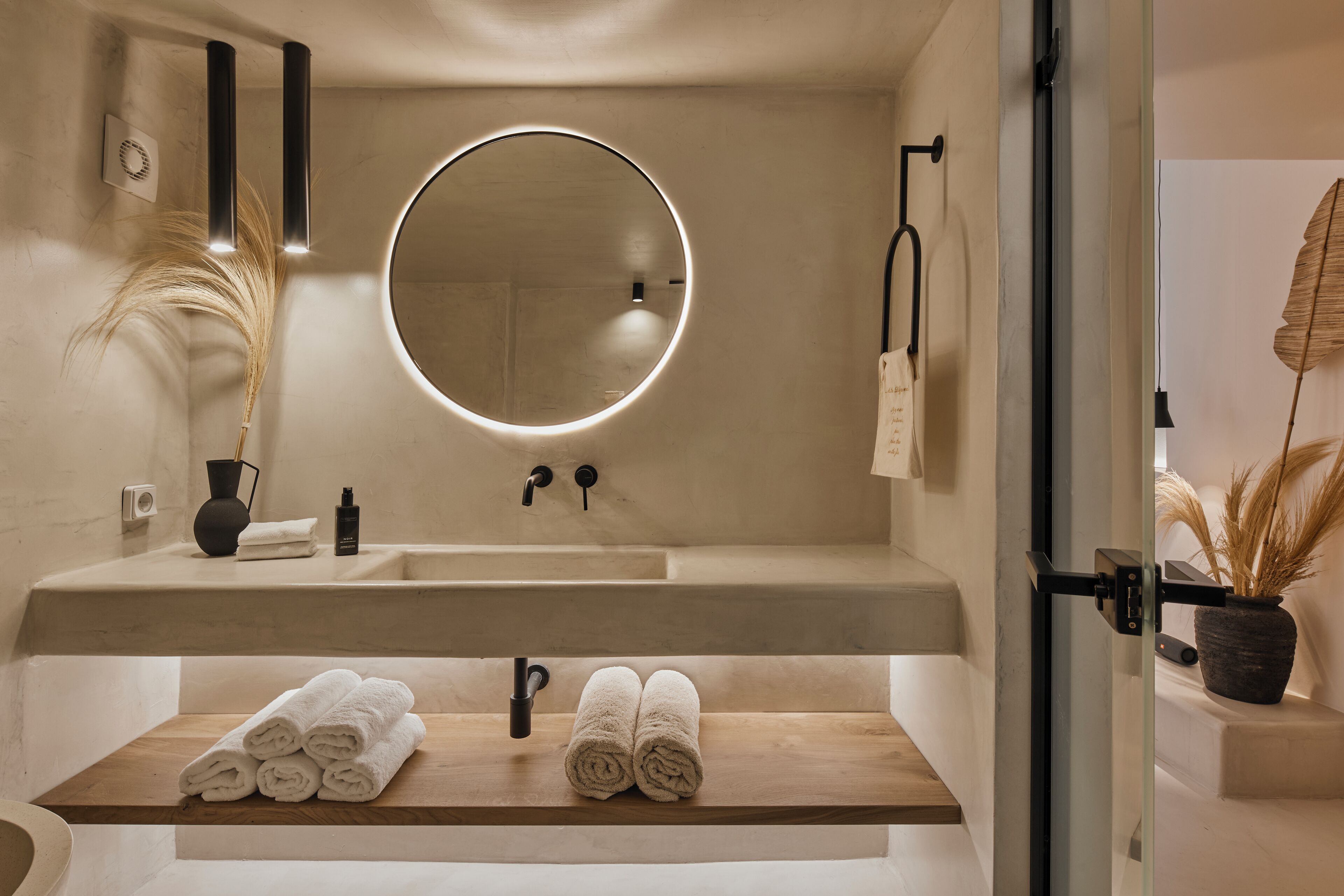 A modern bathroom with a round mirror, a wooden vanity, and neatly rolled towels.