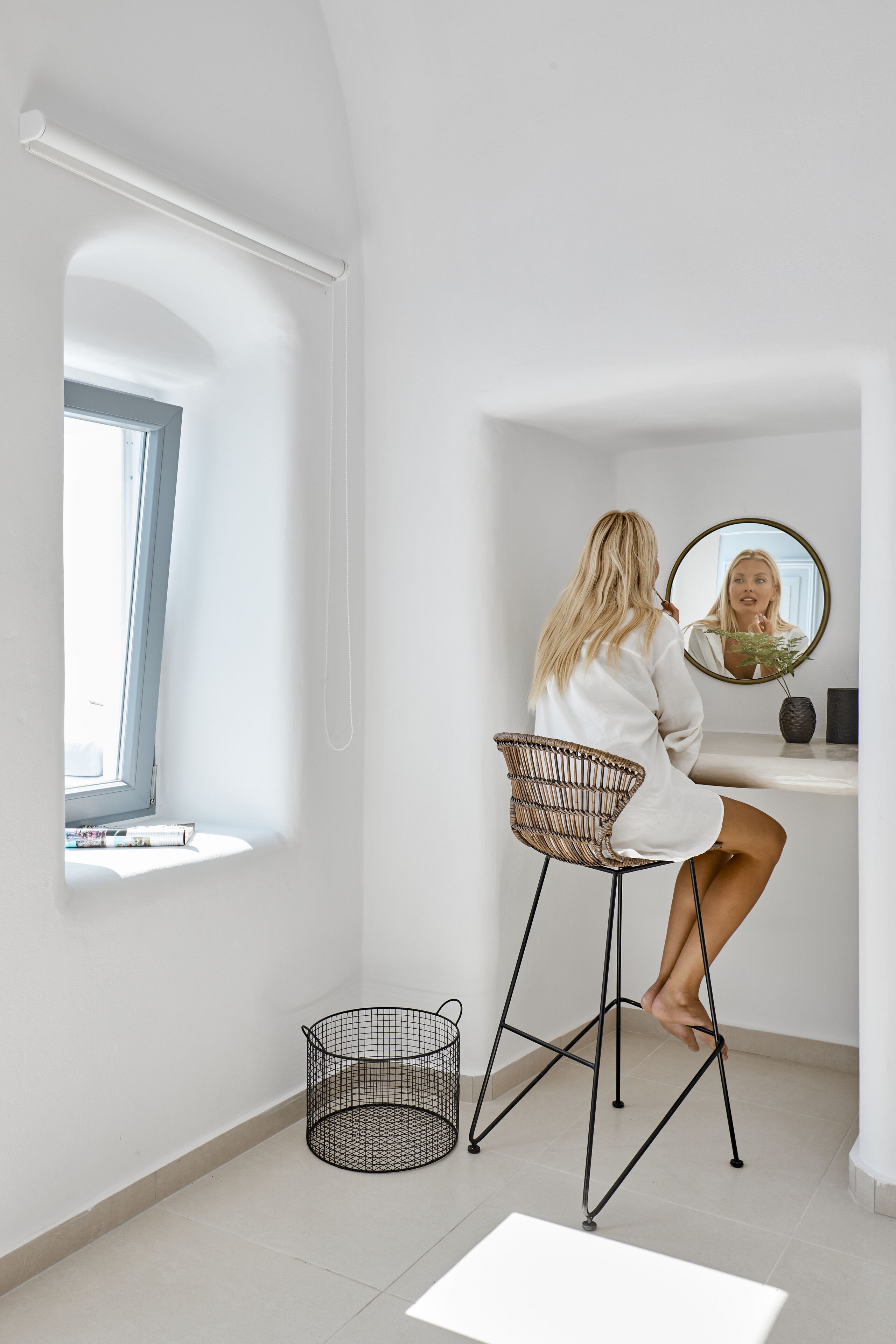 A room with a white interior, a window, a chair, a mirror, and a small table.
