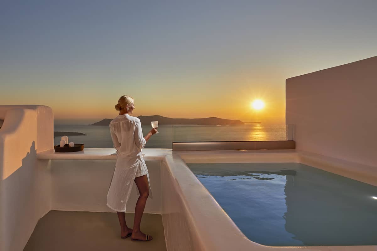 A person in a white robe standing by a pool with a sunset view.