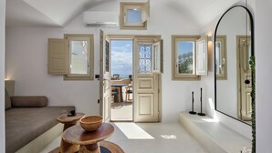 A modern interior with a sofa, wooden tables, and a view through an open door. - You And Me Suites (Santorini)