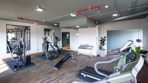 Une salle de sport équipée de divers appareils d’exercice, notamment des tapis de course et des appareils de musculation, et dotée d’un mur entièrement recouvert de miroirs.