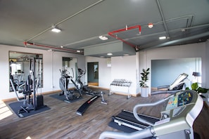 Une salle de sport équipée de divers appareils d’exercice, notamment des tapis de course et des appareils de musculation, et dotée d’un mur entièrement recouvert de miroirs.