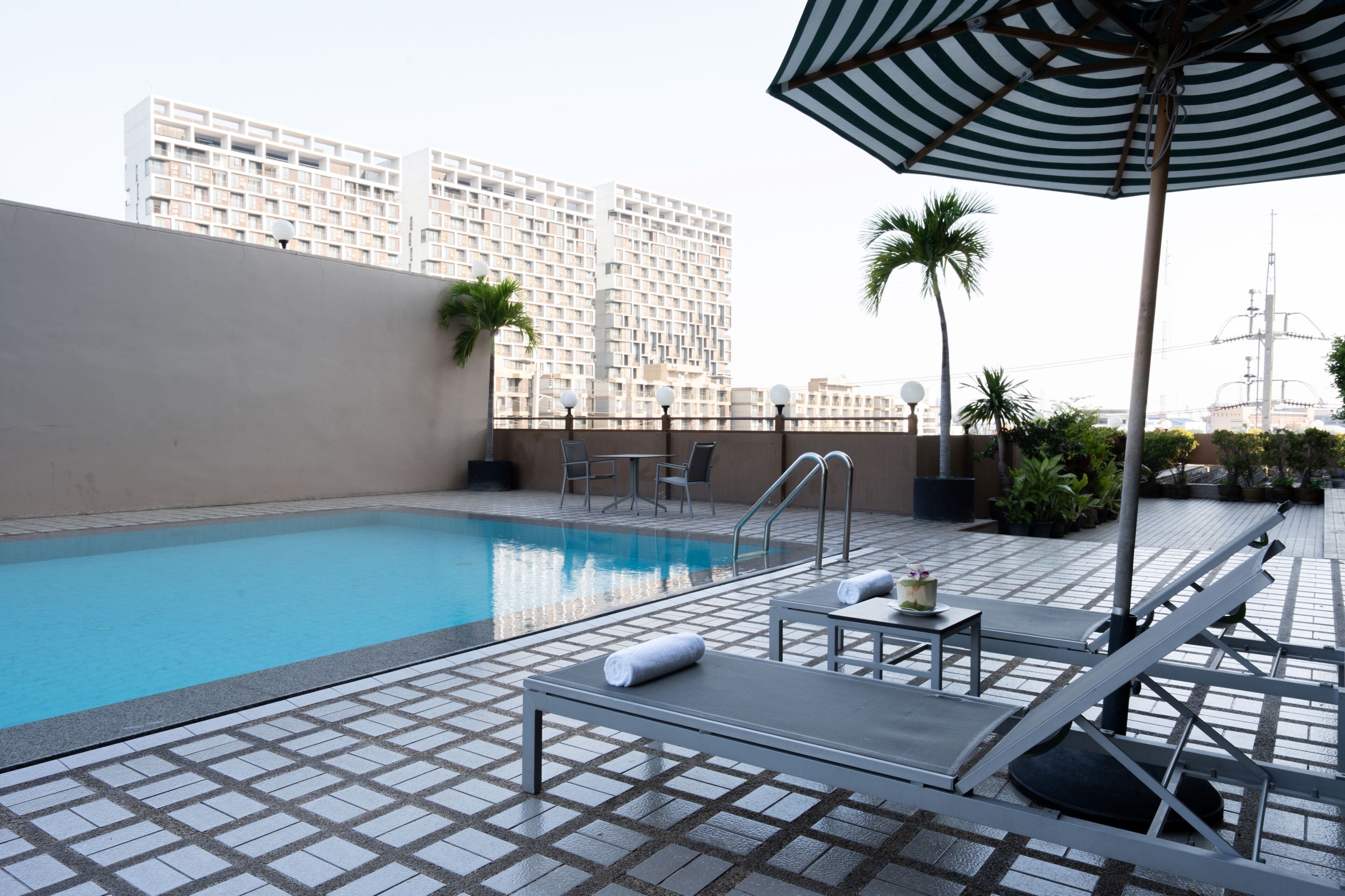Una piscina en la azotea con sillas de descanso, un parasol a rayas y vistas de un rascacielos.