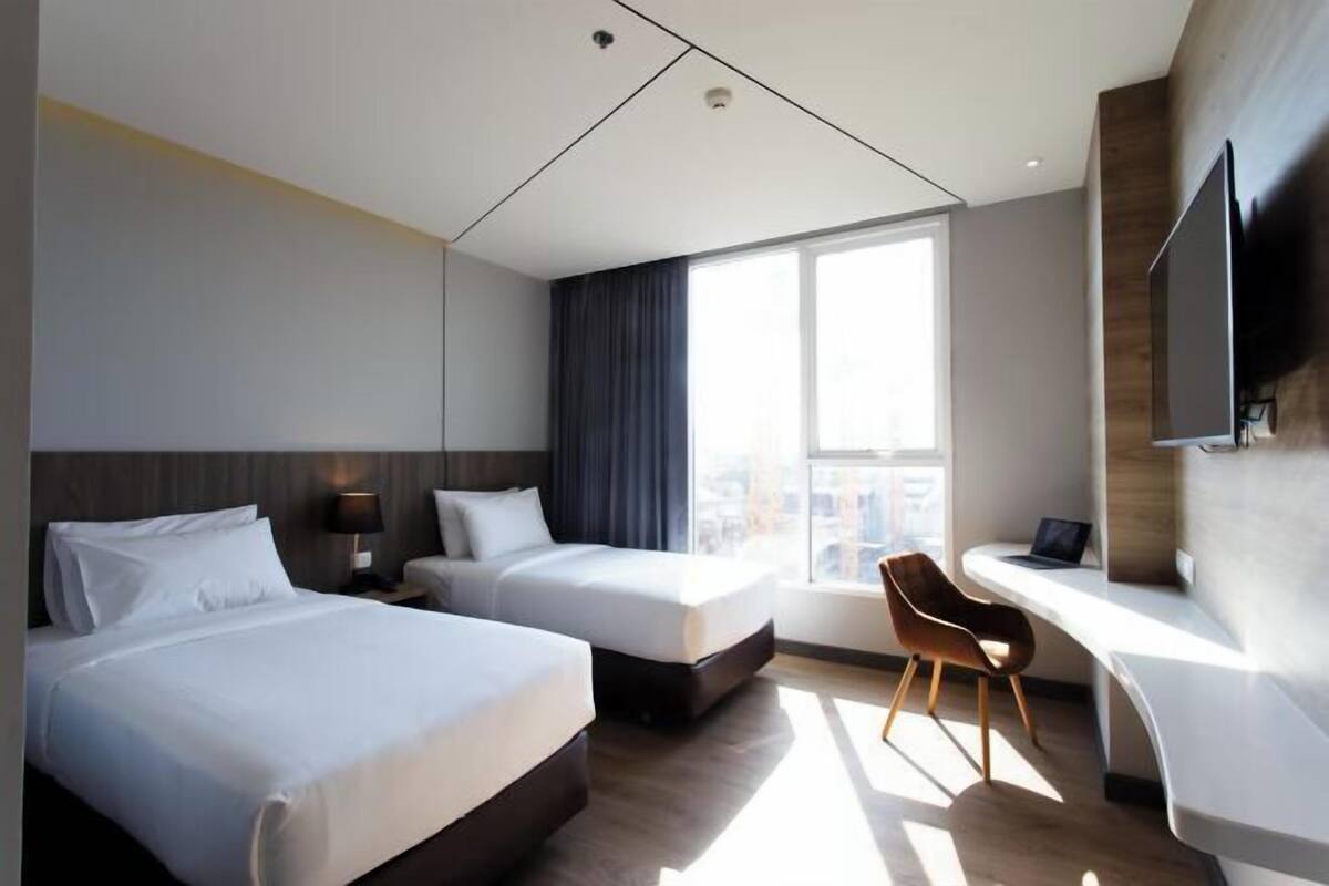 Une chambre d’hôtel moderne équipée de deux lits, d’un bureau, d’une chaise et d’une grande fenêtre.