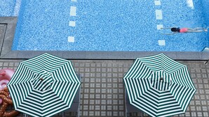 Une piscine agrémentée de deux parasols à rayures vertes et blanches et d’un flotteur.