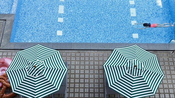 Une piscine agrémentée de deux parasols à rayures vertes et blanches et d’un flotteur.