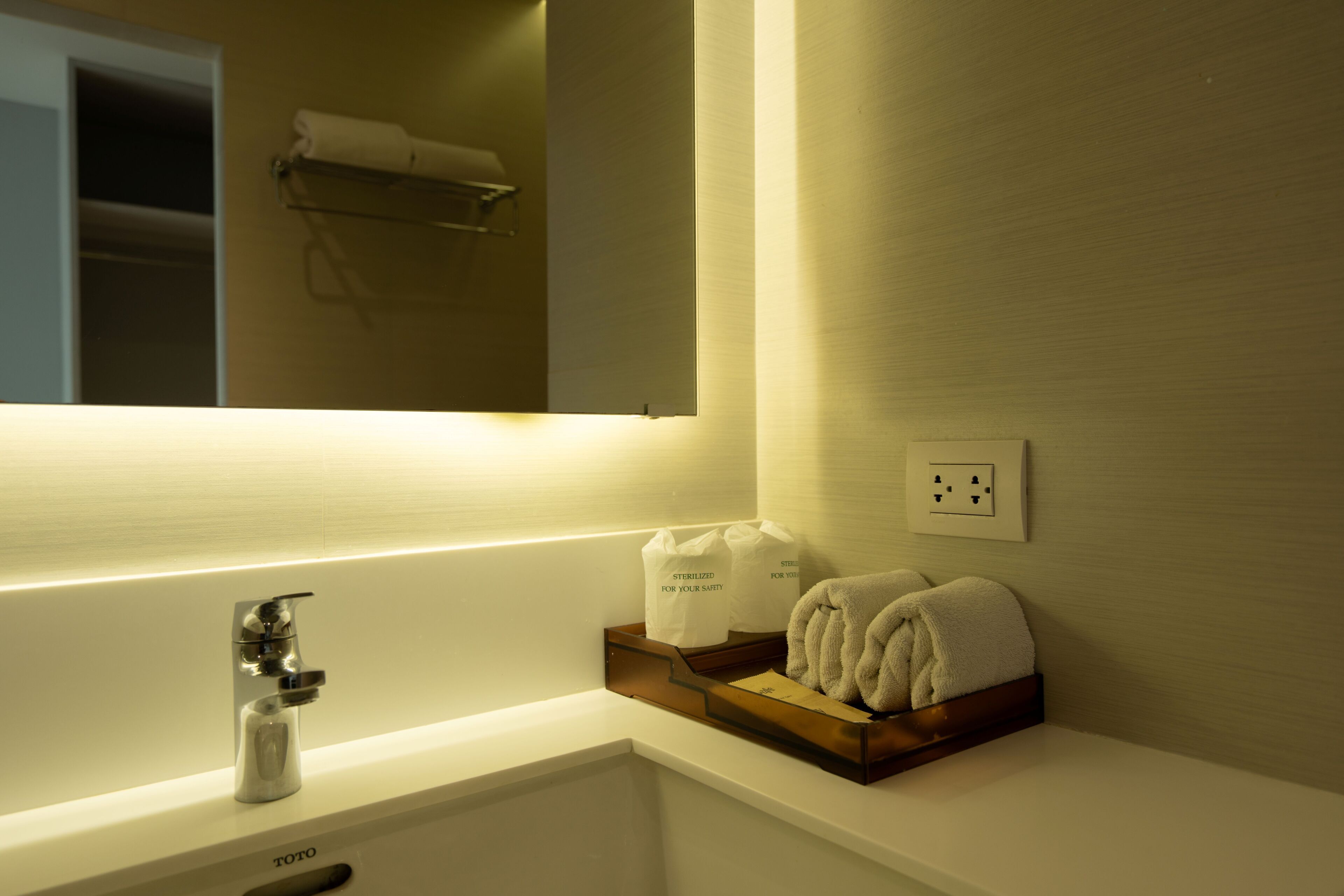 A hotel bathroom with a white sink, a mirror, and a towel rack.