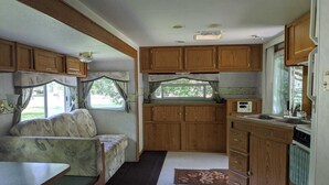 A compact RV interior with a kitchenette, a dining area, and a seating space with a view of the outdoors. - Modern Rental Trailer at Bon Echo Family Campground (The Prowler) (Cloyne)