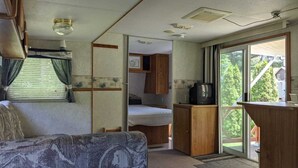 A compact RV interior with a bed, kitchenette, and a small TV. - Modern Rental Trailer at Bon Echo Family Campground (The Prowler) (Cloyne)