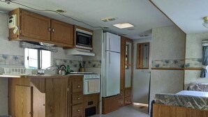A compact RV kitchen with wooden cabinets, a microwave, a stove, and a refrigerator. - Modern Rental Trailer at Bon Echo Family Campground (The Prowler) (Cloyne)