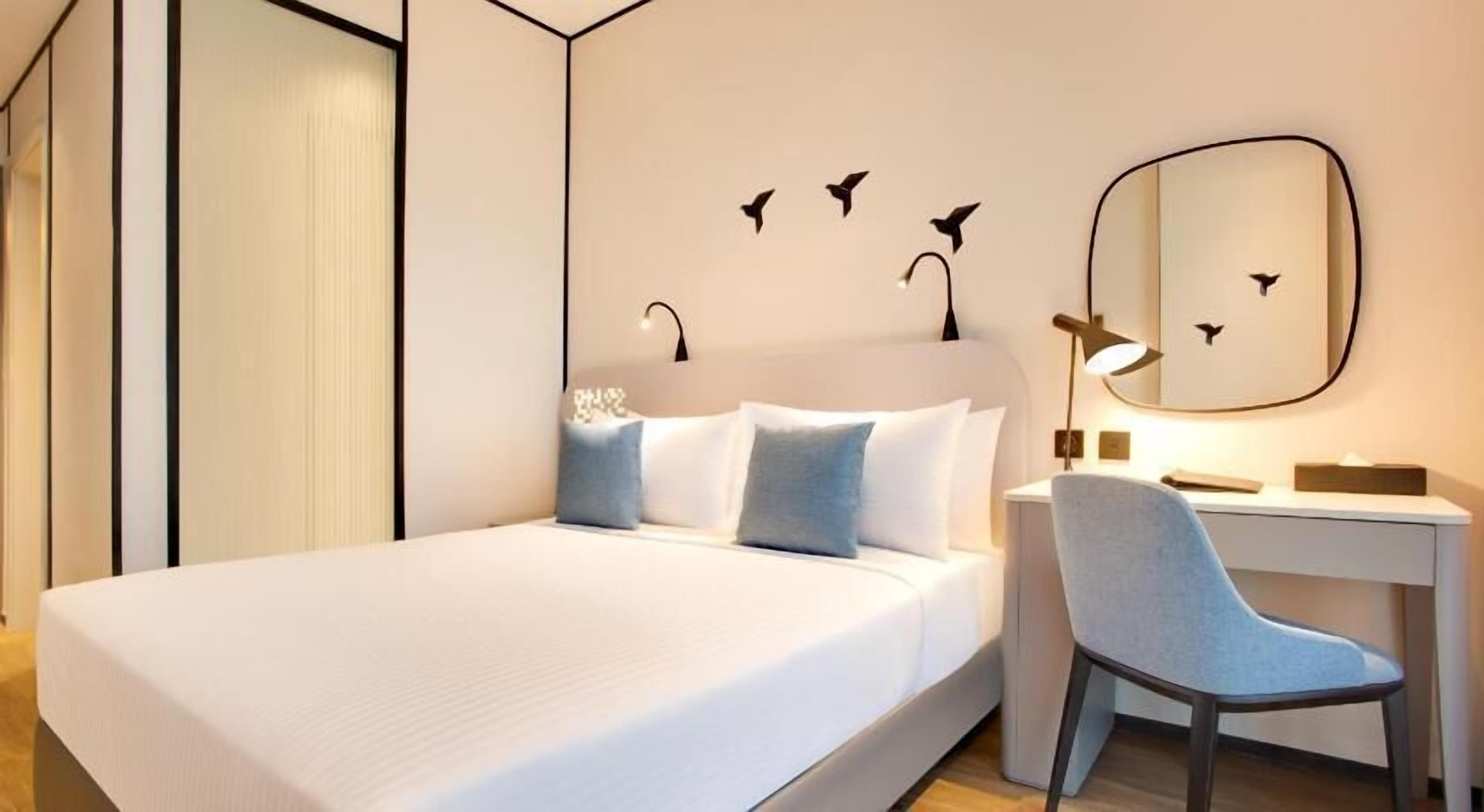 A hotel room with a bed, a desk, a chair, and wall art.