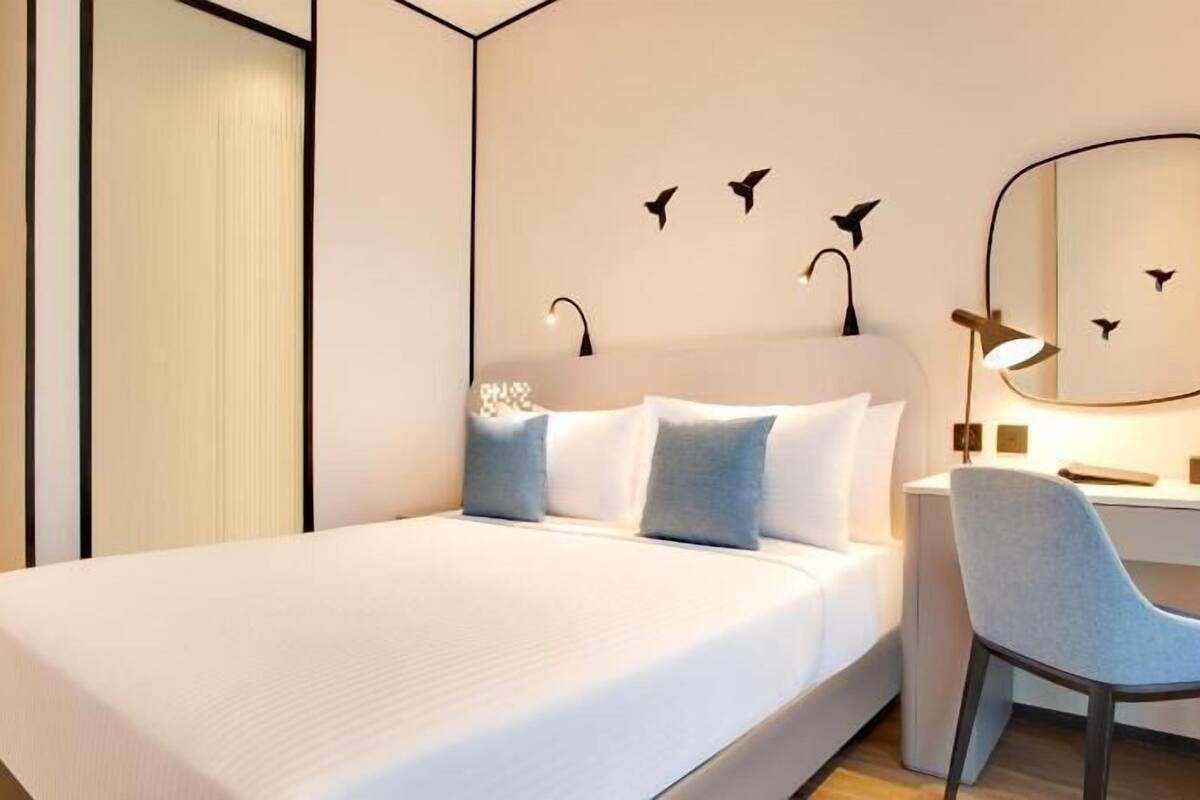 A hotel room with a bed, a desk, a chair, and wall art.