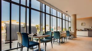 A modern dining area with large windows, multiple tables, and chairs. - The District Hotel (Dubai)