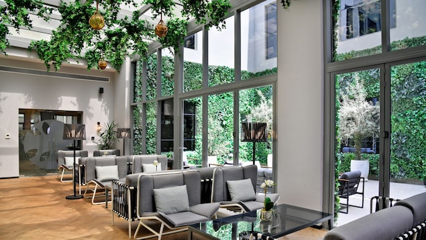 A modern indoor space with a glass table and chairs, a sofa area, and large windows overlooking a garden. - The District Hotel (Dubai)