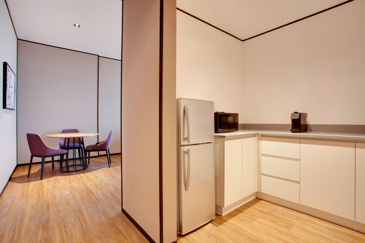 Eine moderne Küche mit weißen Schränken, einem Kühlschrank, einer Mikrowelle und einem Essbereich mit violetten Stühlen und einem Holztisch.