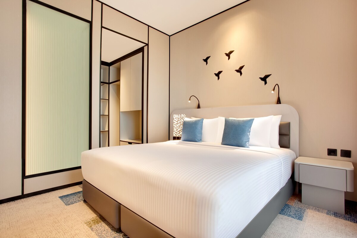 Ein modernes Hotelzimmer mit einem großen Bett, einem begehbaren Kleiderschrank und einer wandmontierten Lampe.