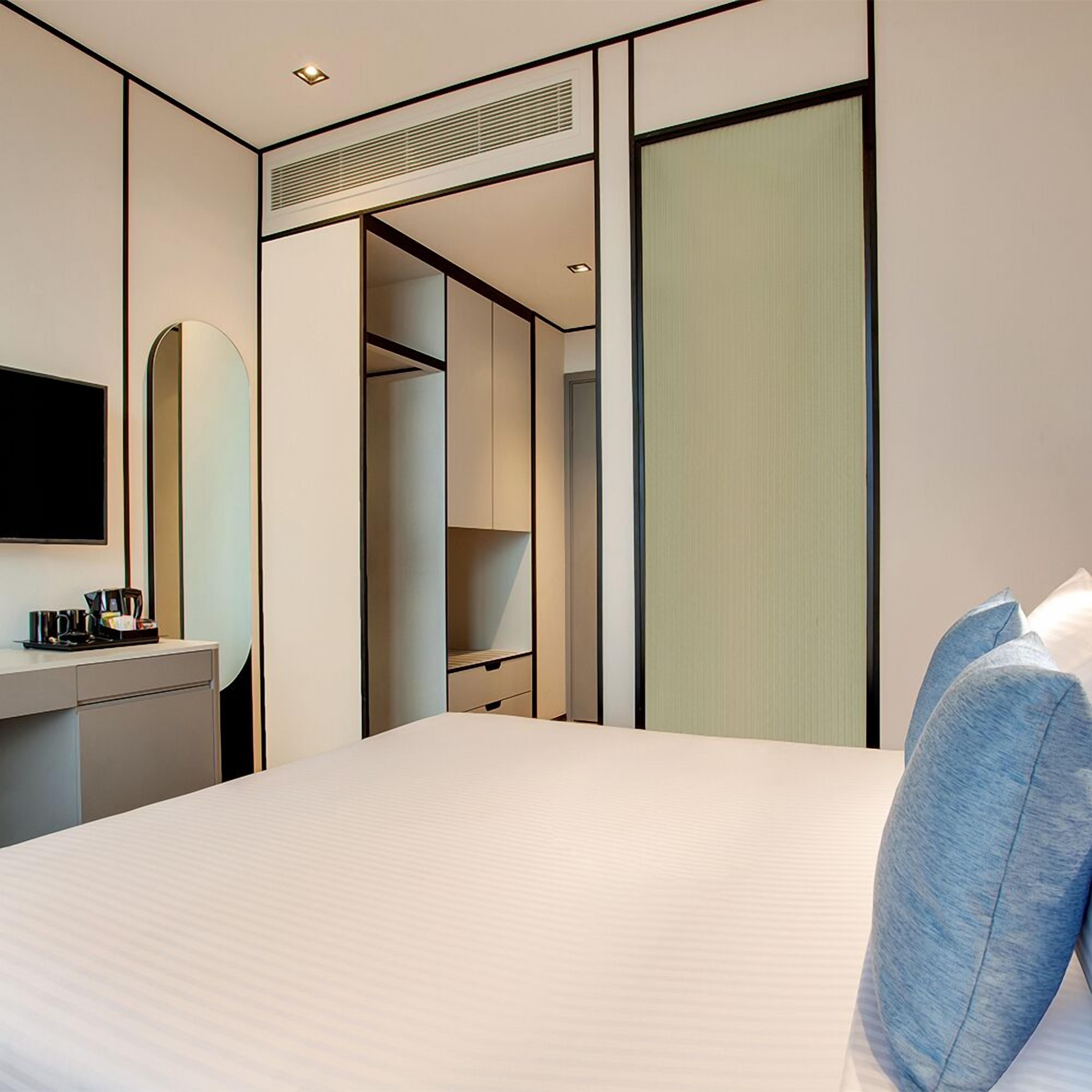 A hotel room with a bed, a desk with a coffee maker, a mirror, a wardrobe, and a television.