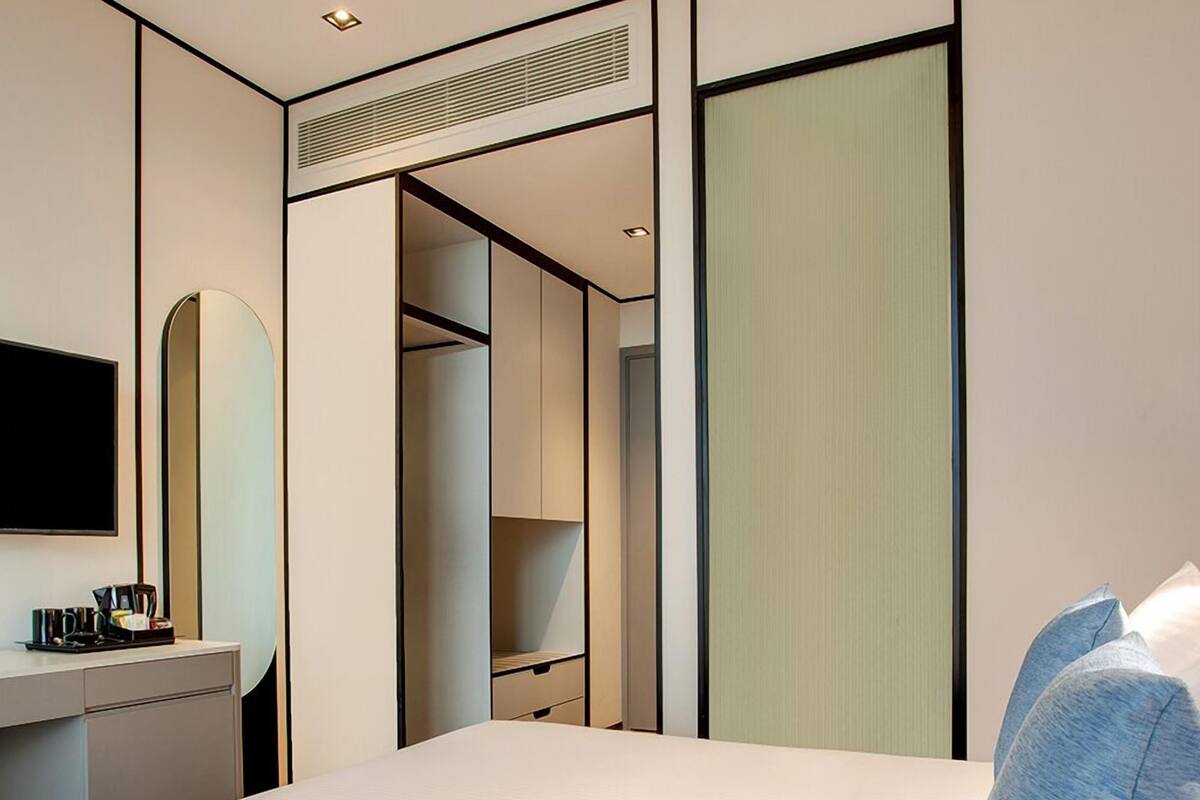 A hotel room with a bed, a desk with a coffee maker, a mirror, a wardrobe, and a television.