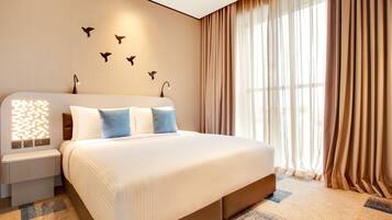 A modern hotel room with a large bed, a nightstand, a wall-mounted light, and a window with curtains.
